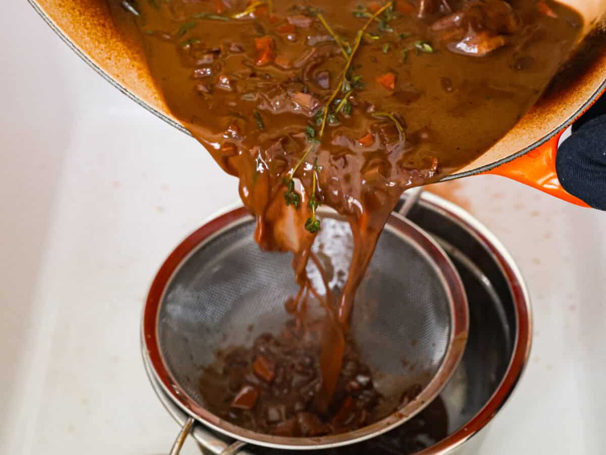 Tender braised short ribs will fall off the bone and leave you speechless! Seared then cooked in a red wine reduction, beef broth, and fresh herbs. Every bite is tender perfection and will melt in your mouth! Seventh photo of the liquid straining from the pot.