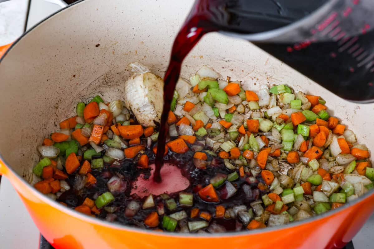 Tender braised short ribs will fall off the bone and leave you speechless! Seared then cooked in a red wine reduction, beef broth, and fresh herbs. Every bite is tender perfection and will melt in your mouth! Fifth photo of the red wine pouring into the pot.