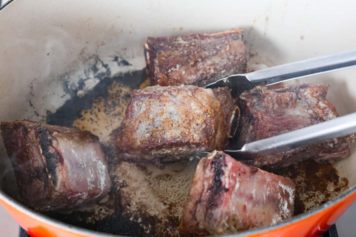 Tender braised short ribs will fall off the bone and leave you speechless! Seared then cooked in a red wine reduction, beef broth, and fresh herbs. Every bite is tender perfection and will melt in your mouth! Third photo of the ribs searing.