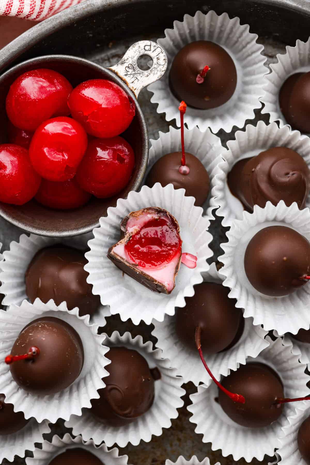 Homemade cherry cordials are a tasty, nostalgic treat! They're made with sweet cherries that are coated in a rich chocolate shell. Make them for Christmas or Valentineโs Day, and watch them disappear! Overhead shot of cherry cordials in paper wrappers with one that has a bite taken out.