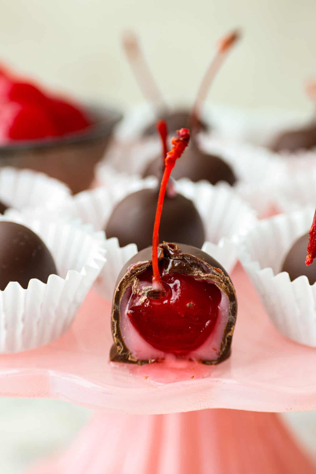 Homemade cherry cordials are a tasty, nostalgic treat! They're made with sweet cherries that are coated in a rich chocolate shell. Make them for Christmas or Valentineโs Day, and watch them disappear! Close up shot of a cherry cordial with a bite taken out of it.
