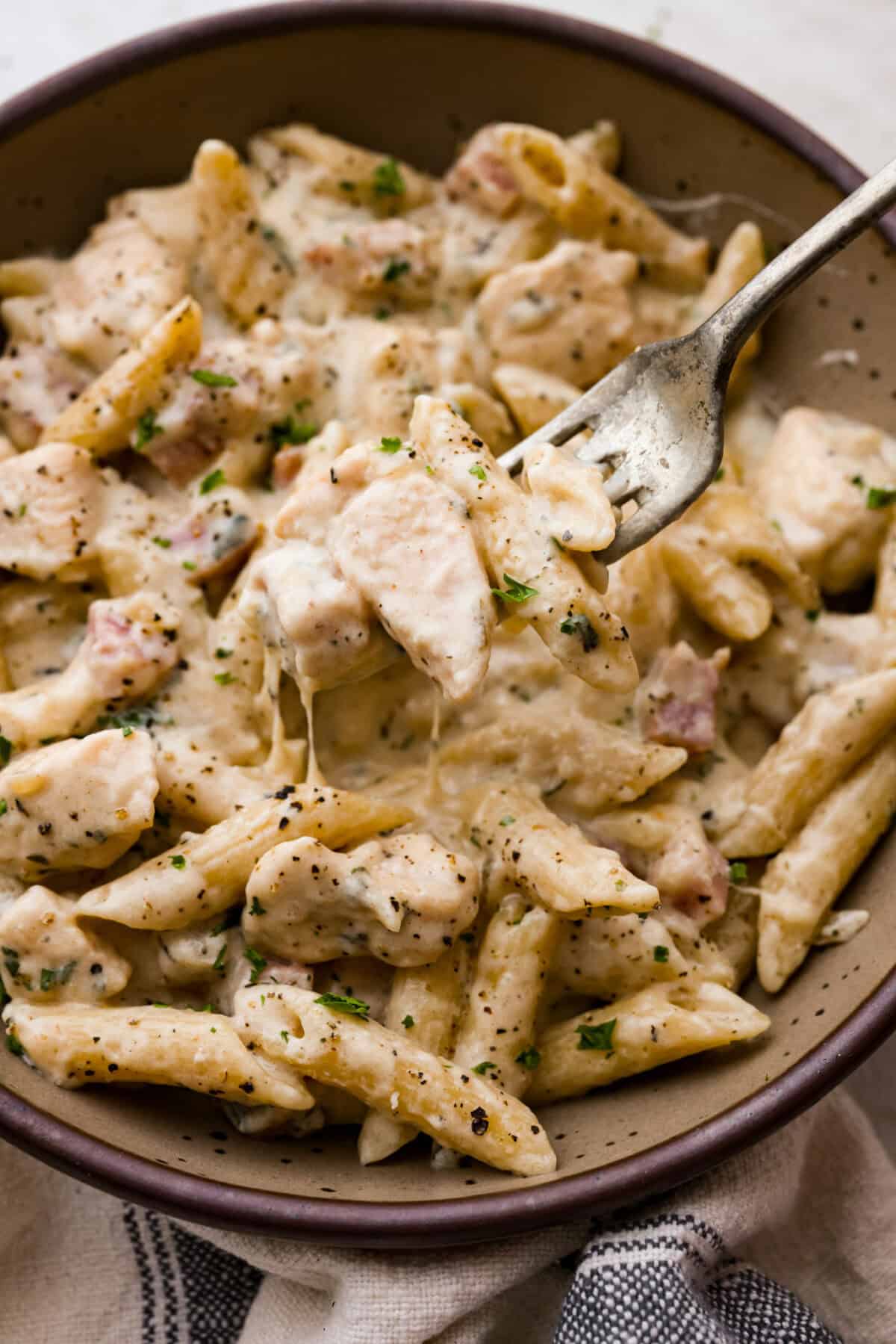 Chicken cordon bleu pasta is a creamy, flavorful dish that's a fun twist on the classic. It combines savory ham, tender chicken, melty cheese, and delicious seasonings. Easy to make and sure to please! Close up shot of a fork full of a bite chicken cordon bleu pasta.