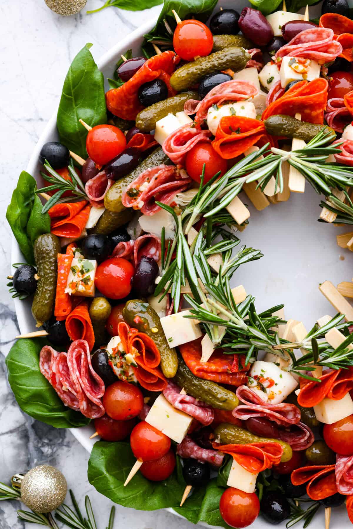 Bring this antipasto charcuterie wreath to your next holiday party! Skewered cheese, deli meats, olives, and pickles shaped into a cute Christmas wreath. A perfect festive appetizer to impress your guests! Close view of antipasto charcuterie skewers.