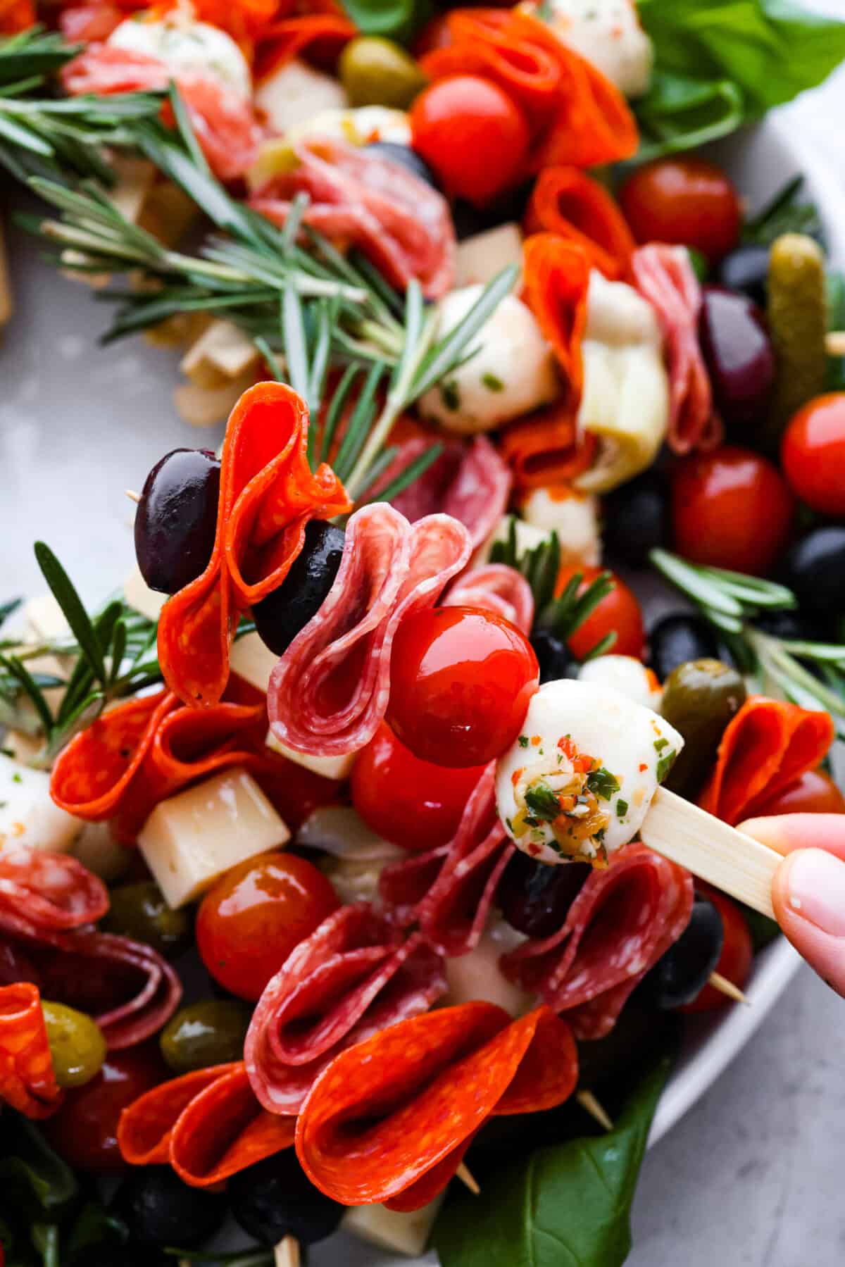 Bring this antipasto charcuterie wreath to your next holiday party! Skewered cheese, deli meats, olives, and pickles shaped into a cute Christmas wreath. A perfect festive appetizer to impress your guests! Close view of a skewer full of antipasto ingredients.