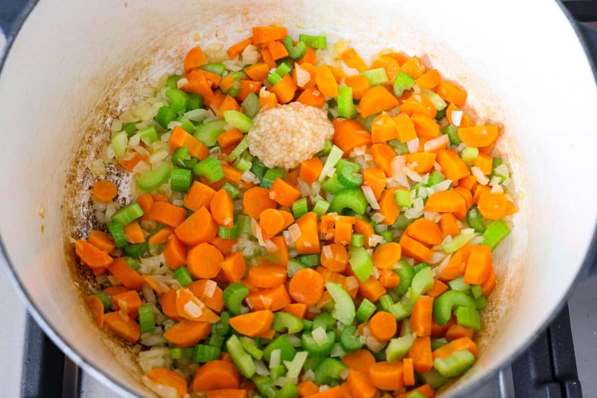 This crack chicken noodle soup is absolutely irresistible! It's packed with shredded chicken, bacon, ranch seasonings, and noodles, all in a deliciously creamy broth. One bite, and you'll be hooked! Overhead shot of carrots, celery and onions in the bottom of a pot with garlic on top.