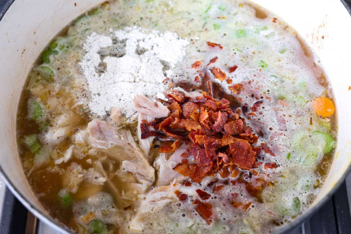 This crack chicken noodle soup is absolutely irresistible! It's packed with shredded chicken, bacon, ranch seasonings, and noodles, all in a deliciously creamy broth. One bite, and you'll be hooked! Overhead shot of broth, ranch packet, shredded chicken and bacon in the same pot with the veggies.
