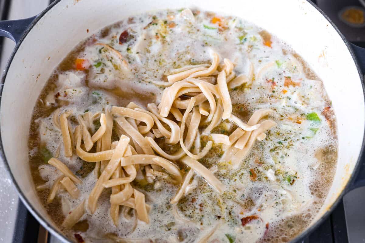 This crack chicken noodle soup is absolutely irresistible! It's packed with shredded chicken, bacon, ranch seasonings, and noodles, all in a deliciously creamy broth. One bite, and you'll be hooked! Overhead shot of noodles added in with the broth, chicken, bacon seasoning and veggies.