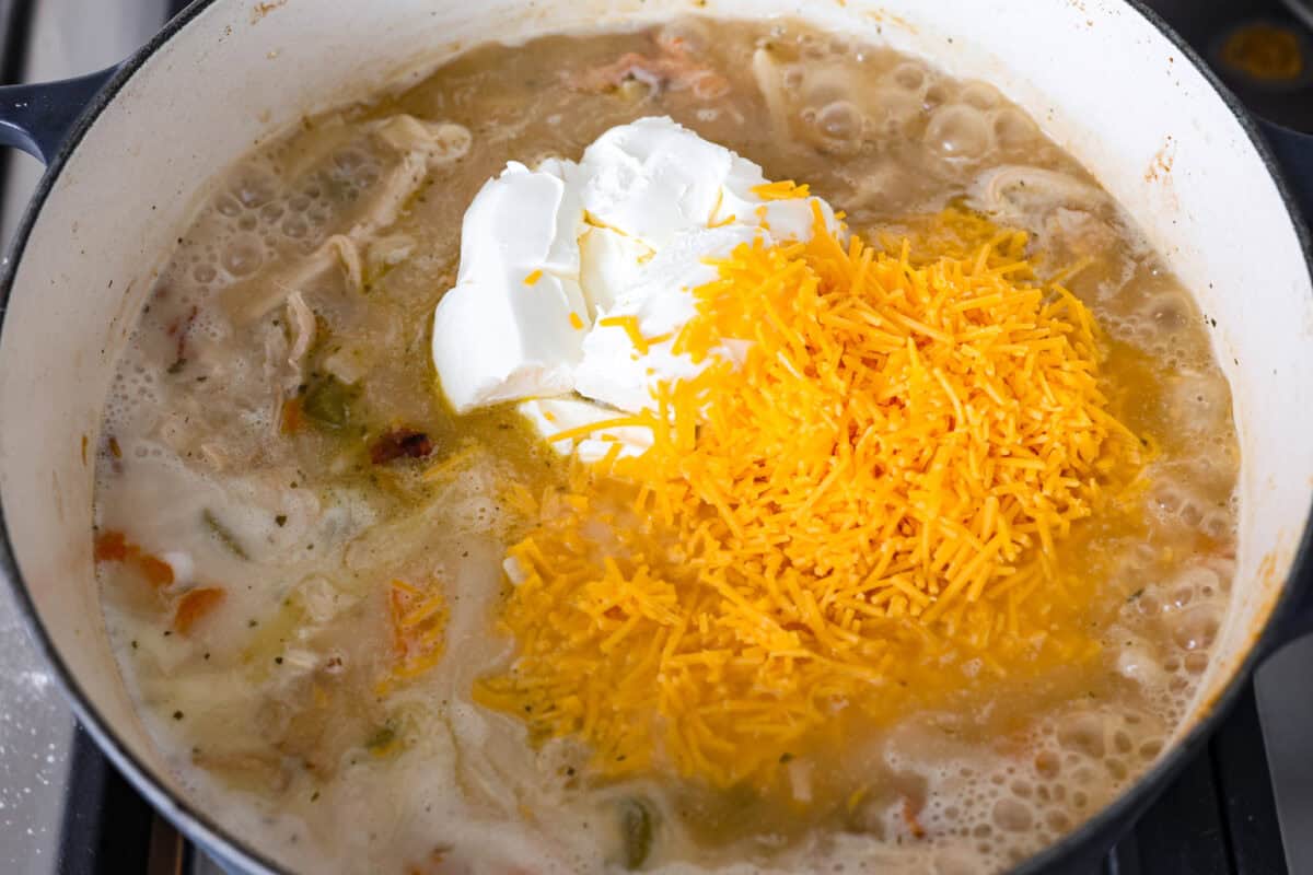 This crack chicken noodle soup is absolutely irresistible! It's packed with shredded chicken, bacon, ranch seasonings, and noodles, all in a deliciously creamy broth. One bite, and you'll be hooked! Overhead shot of cream cheese and cheddar cheese added on top of the rest of the ingredients.