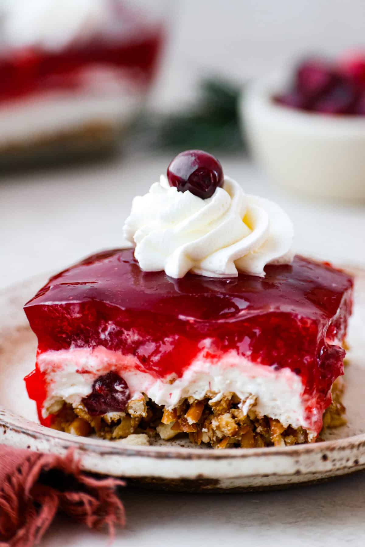 Make this festive cranberry pretzel salad for the holidays! The salty pretzel crust is the perfect balance to the sweet and creamy layers. Cranberry sauce gives it a pop of tartness and makes it holiday-ready! Close view of a slice of cranberry pretzel salad on a plate.