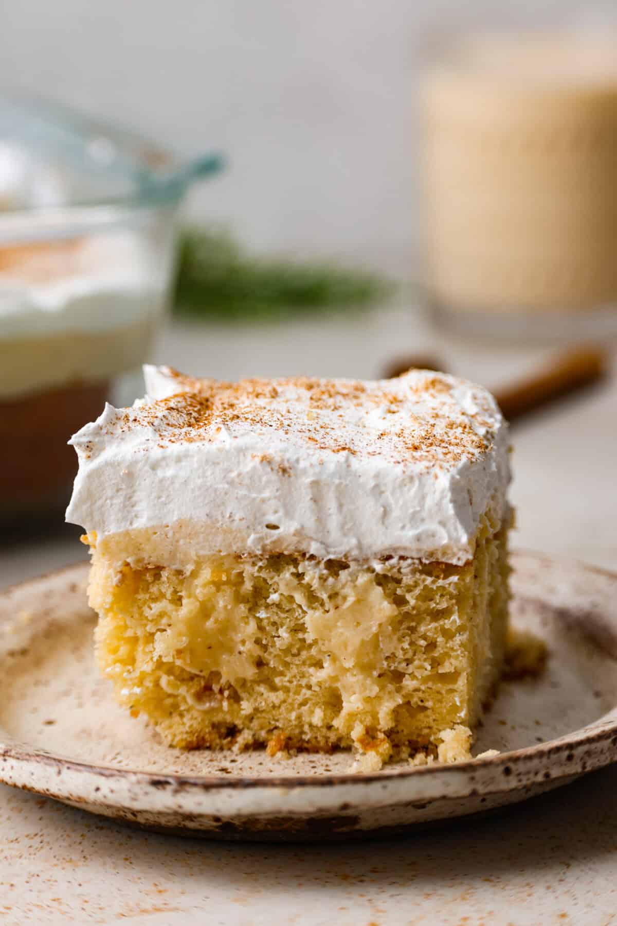 Eggnog Poke Cake could not be more perfect for the holiday season! It combines the rich flavor of eggnog with the soft, moist texture of a classic poke cake. Add fluffy whipped topping and a sprinkle of nutmeg and cinnamon to really wow your family! Side shot of plated eggnog poke cake.