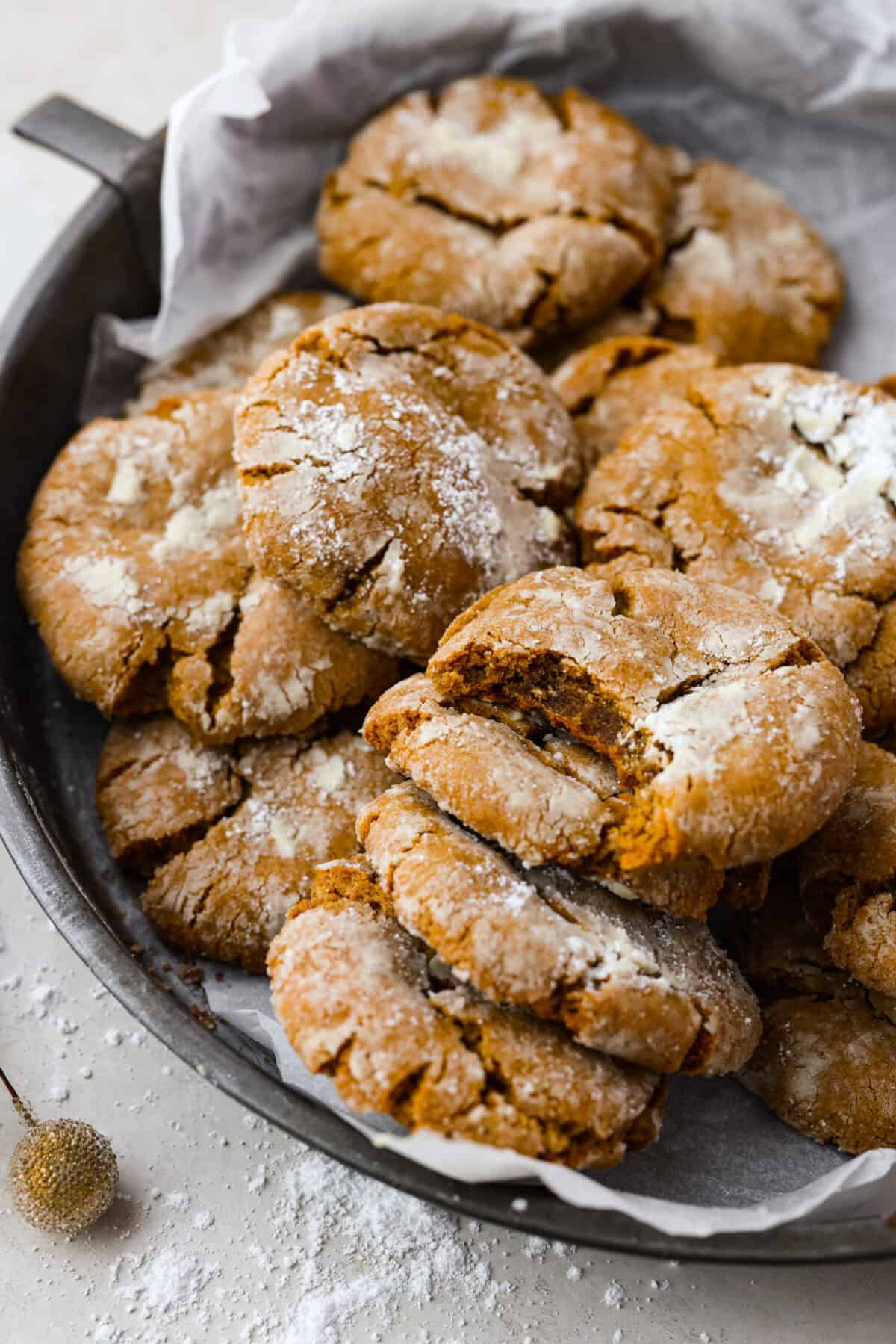 These gingerbread crinkle cookies are incredibly soft and flavorful! Their deep molasses flavor, spiced to perfection and rolled in powdered sugar, is so good with a glass of milk. They are the perfect cookies to make for Santa this holiday season. Close up shot of gingerbread crinkle cookies on a serving plate.