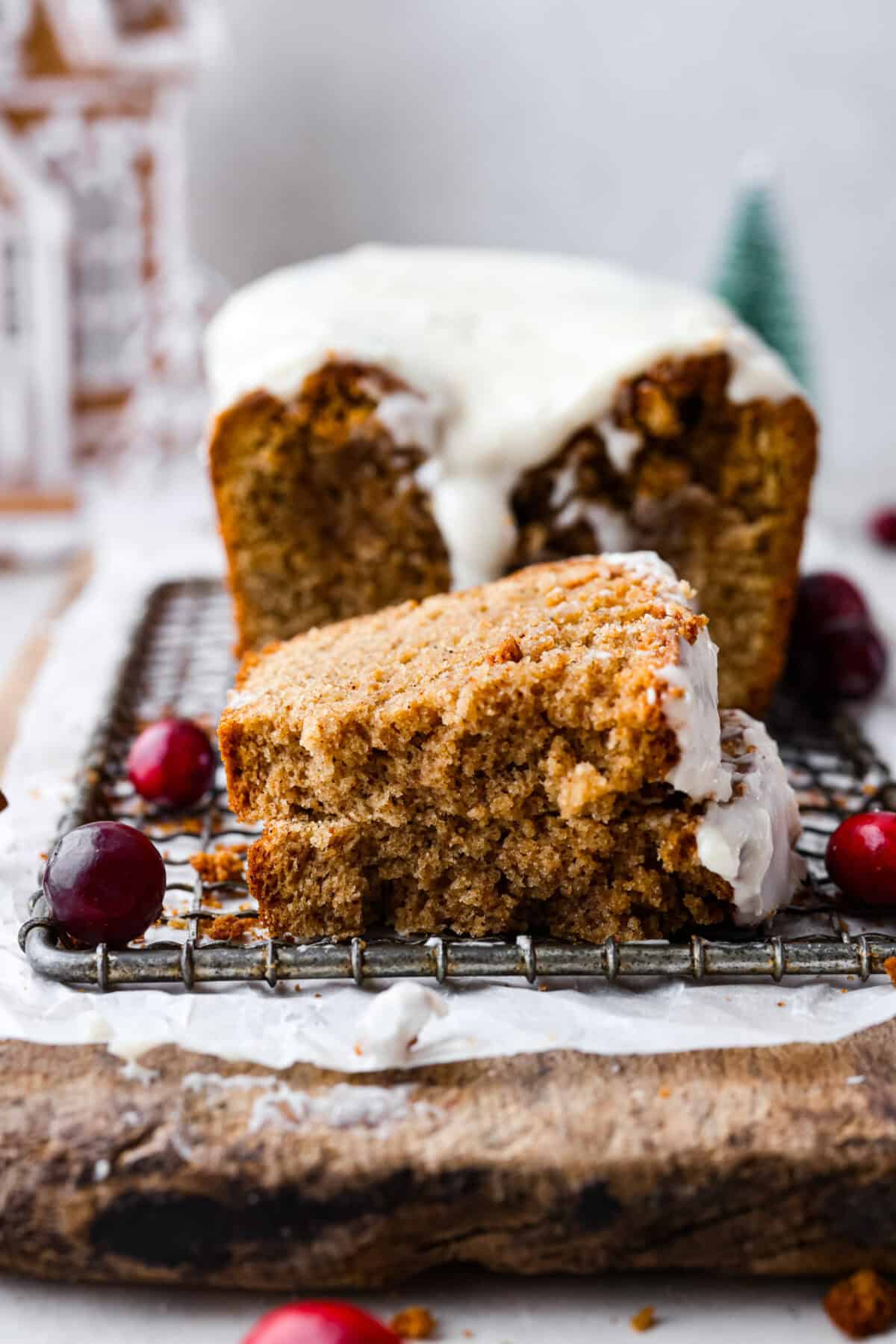 Starbucks copycat gingerbread loaf is the ultimate holiday treat! It's coated in a simple cream cheese frosting and is full of warm spices and rich molasses flavor. Enjoy it for Christmas brunch or a sweet treat at night! Side shot of gingerbread loaf slice torn in half on a cooling rack in front of the whole loaf.