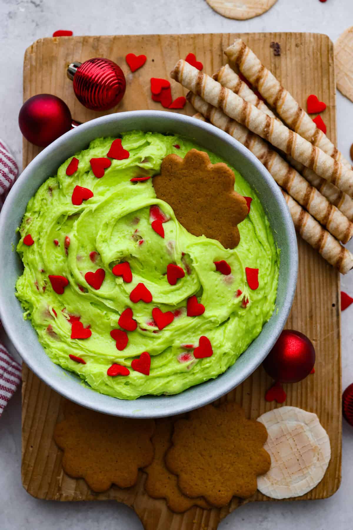 Grinch dip is a sweet and scrumptious dip perfect for any holiday party or gathering. It combines delicious cake mix, fluffy whipped topping, and smooth yogurt or pudding to create a fun dip for cookies, treats, or fruit. Overhead shot of grinch dip in a bowl surrounded by cookies and Christmas items.