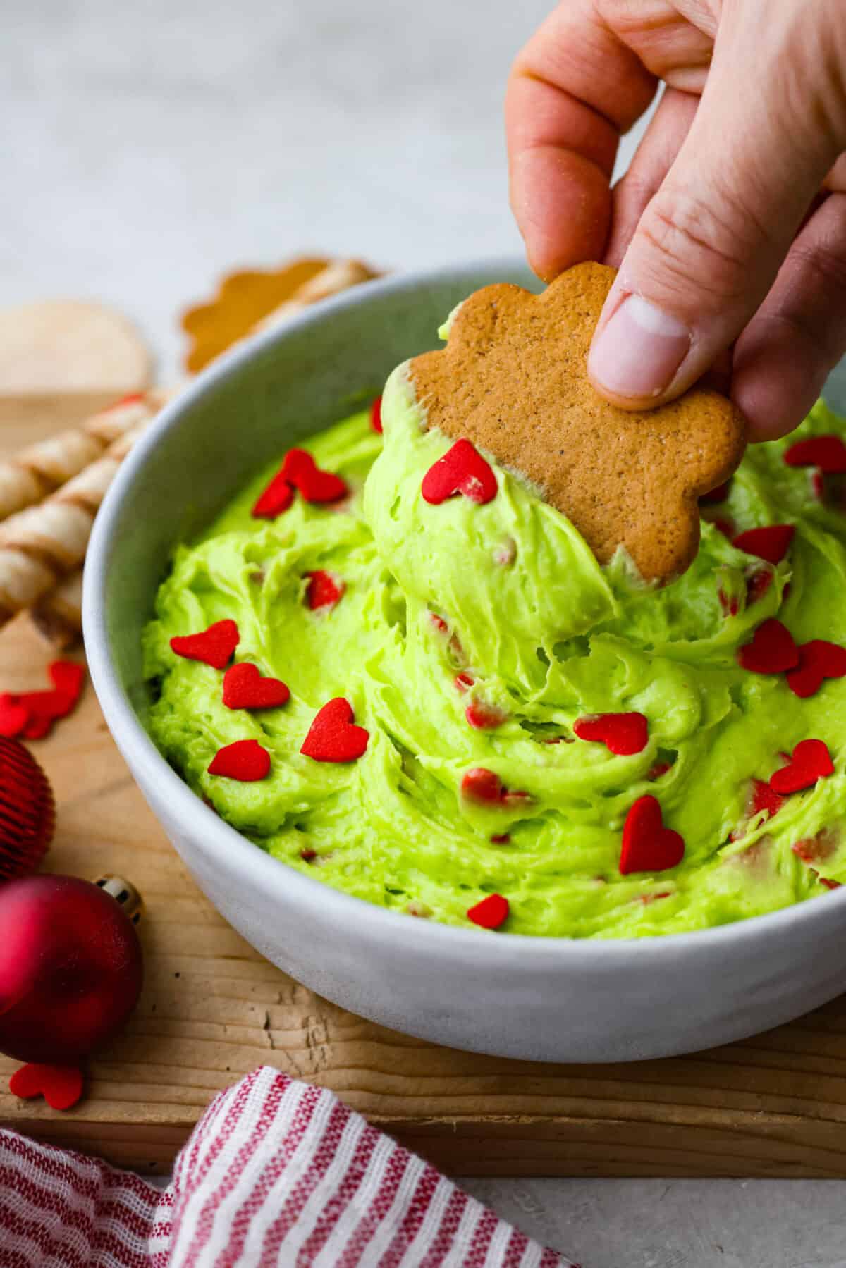 Grinch dip is a sweet and scrumptious dip perfect for any holiday party or gathering. It combines delicious cake mix, fluffy whipped topping, and smooth yogurt or pudding to create a fun dip for cookies, treats, or fruit. Angle shot of someone dipping a cookie into the Grinch Dip.