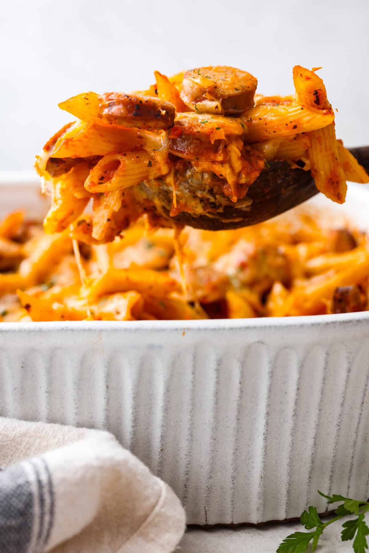 This one-pan Italian Sausage Casserole is the ultimate comfort food! With tender pasta, flavorful sausage, rich marinara, and gooey melted cheese, it’s an easy dinner that’s perfect for busy nights. It's a recipe the whole family will love! Side shot of someone lifting a scoop of Italian sausage casserole out of the dish.