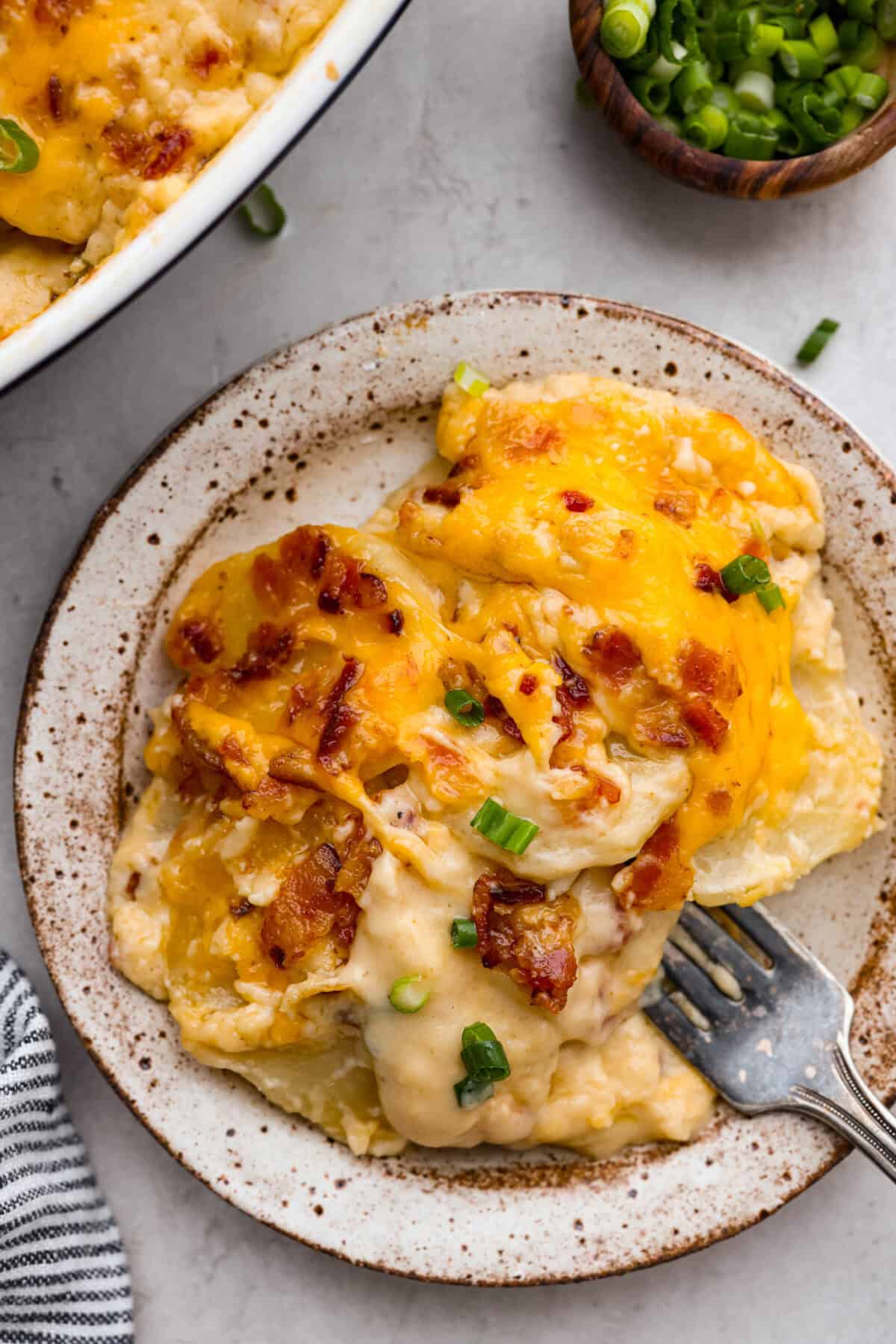Loaded scalloped potatoes are rich, creamy, and "loaded" with flavor! This recipe combines tender potatoes baked to perfection in a velvety sauce topped with crispy bacon, green onions, and melty cheese. Overhead shot of plated loaded scalloped potatoes.
