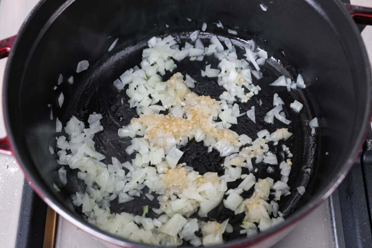 Fall in love with the creamy, comforting flavors in this marry me chicken soup! It's loaded with shredded chicken and tender noodles in a rich and creamy soup base. The irresistible flavors from the sun-dried tomatoes, garlic, and parmesan cheese take this soup over the top! First photo of the onions and garlic sautรฉing in a pot.