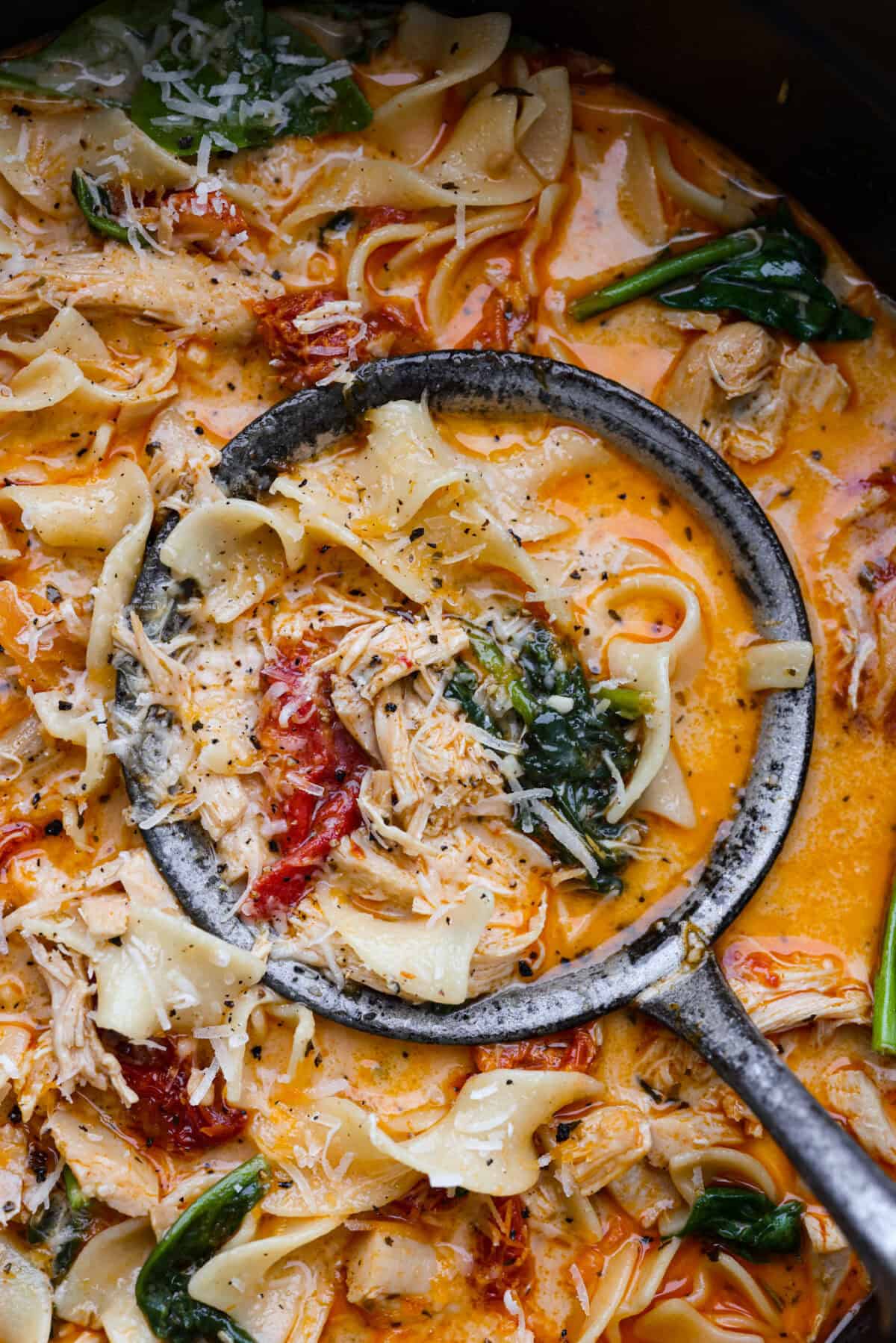 Fall in love with the creamy, comforting flavors in this marry me chicken soup! It's loaded with shredded chicken and tender noodles in a rich and creamy soup base. The irresistible flavors from the sun-dried tomatoes, garlic, and parmesan cheese take this soup over the top! Close view of a ladle full of marry me chicken soup.