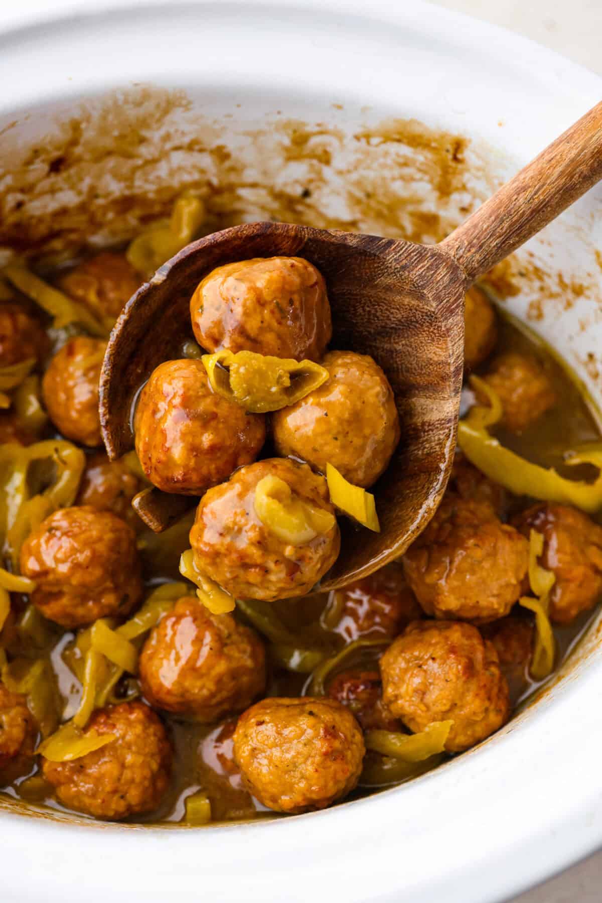 Crockpot Mississippi meatballs make the best little appetizer or side dish. The flavorful pepperoncini mixed with the au jus and ranch seasoning packets with delectable butter makes the most amazing sauce. It's perfectly soaked up by the tender meatballs. Close up shot of crockpot Mississippi meatballs in a wooden serving spoon.