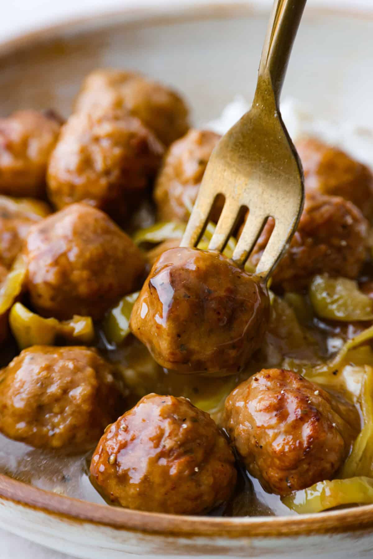Crockpot Mississippi meatballs make the best little appetizer or side dish. The flavorful pepperoncini mixed with the au jus and ranch seasoning packets with delectable butter makes the most amazing sauce. It's perfectly soaked up by the tender meatballs. Close up shot of a gold fork with a crockpot Mississippi meatball skewered on the end.