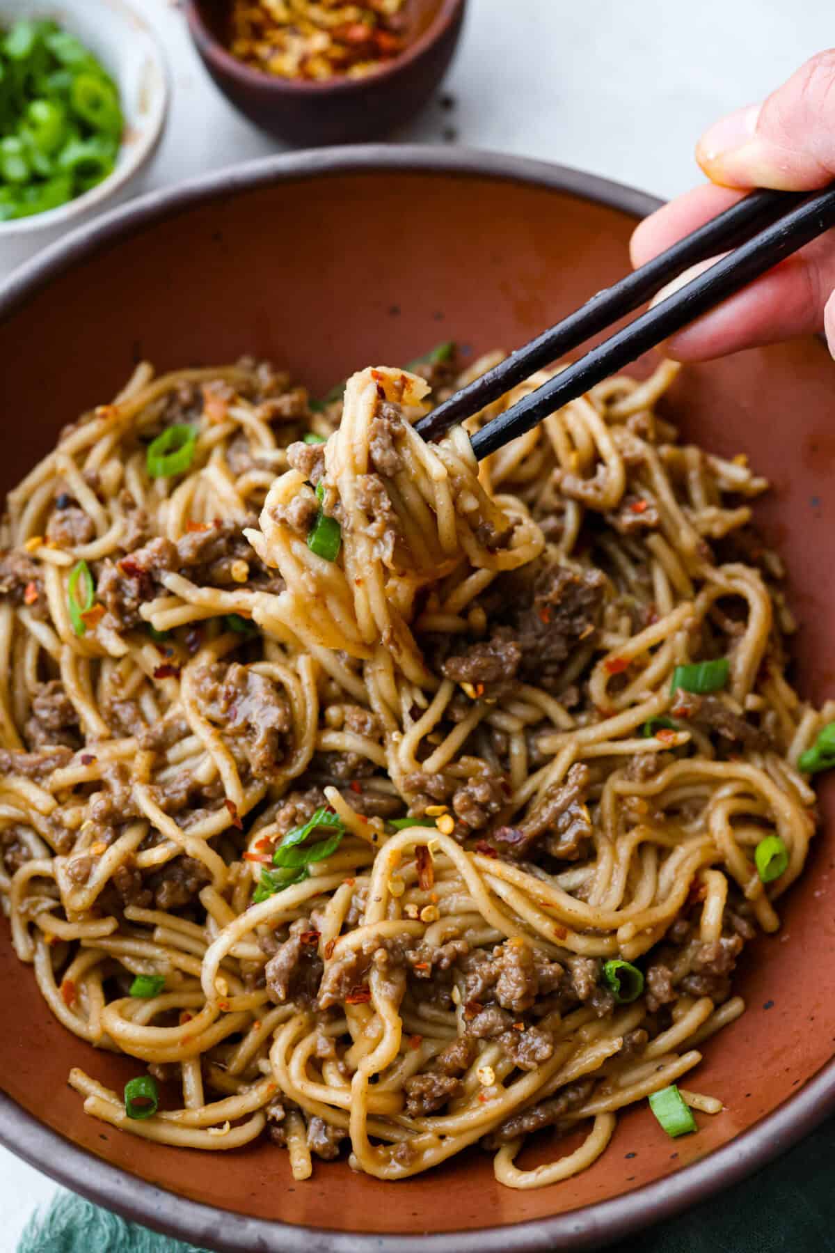 Mongolian Ground Beef and Noodles is a flavorful dinner that’s ready in 30 minutes! This dish combines tender noodles, savory ground beef, and a sweet and tangy Asian-inspired sauce for a meal that’s as comforting as it is delicious! Angle shot of someone getting a bite with Mongolian ground Beef and Noodles.