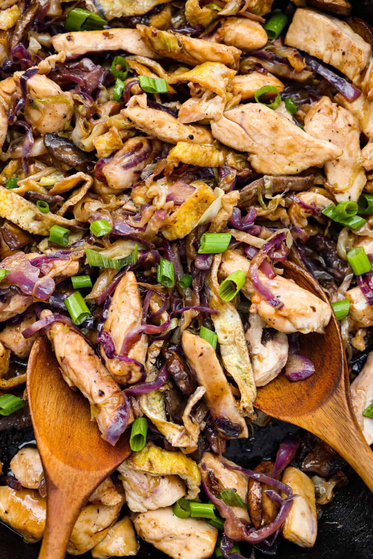 Moo Shu Chicken is a takeout favorite that’s so easy to make at home! This flavorful dish combines tender strips of chicken, mushrooms, and cabbage with a sweet and savory sauce. It’s quick, packed with vibrant flavors, and the perfect weeknight meal! Close up shot of Moo Shu Chicken with two wooden serving spoons.