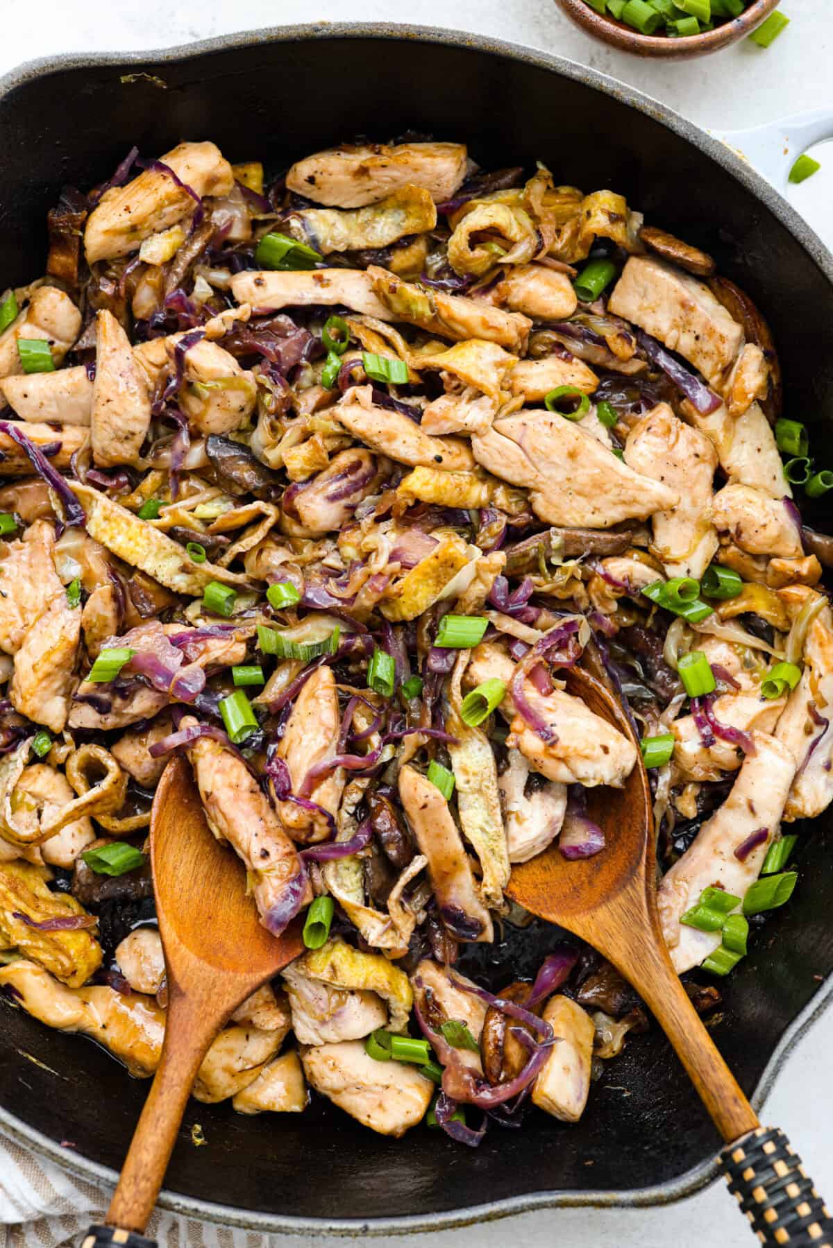 Moo Shu Chicken is a takeout favorite that’s so easy to make at home! This flavorful dish combines tender strips of chicken, mushrooms, and cabbage with a sweet and savory sauce. It’s quick, packed with vibrant flavors, and the perfect weeknight meal! Overhead shot of Moo Shu chicken in a skillet.