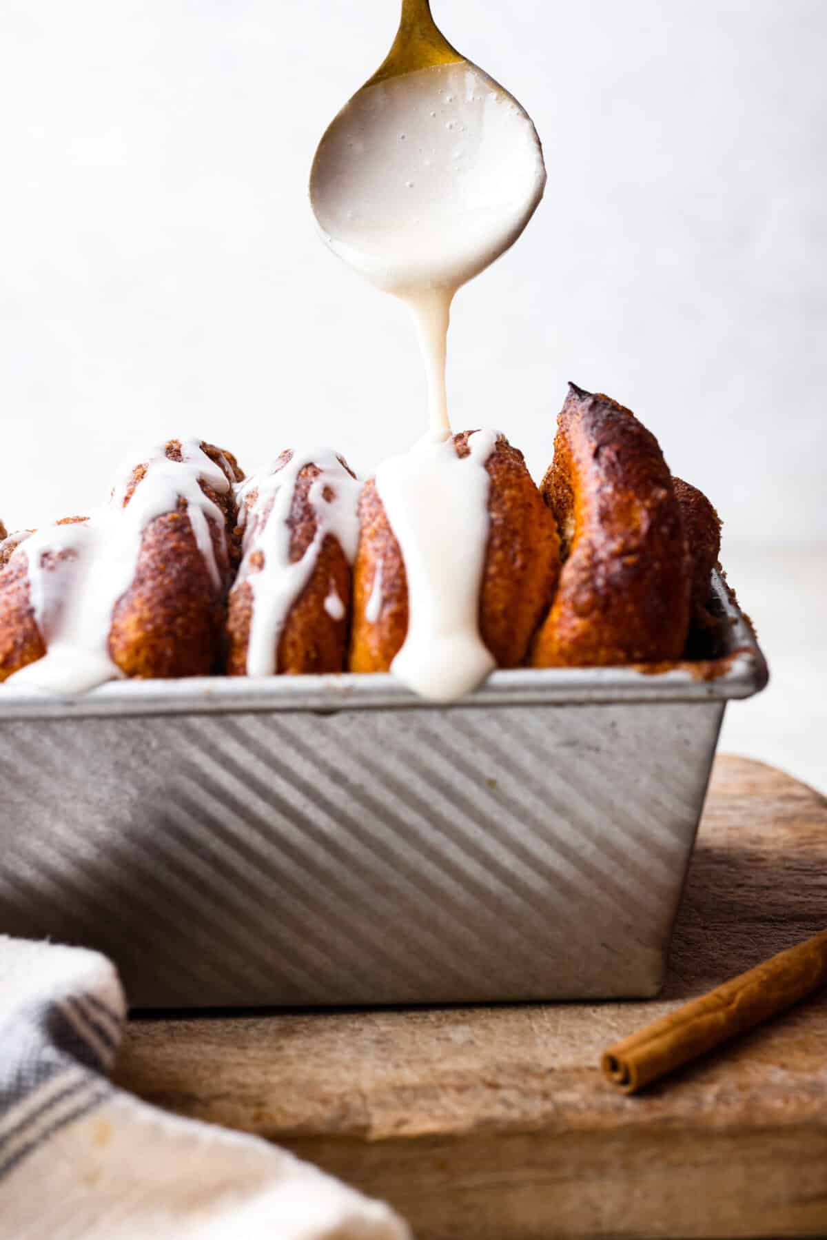 Irresistible Cinnamon Pull-Apart Bread is inspired by the popular cinnamon bread served at the Grist Mill eatery in Dollywood. With this copycat version, you can recreate that buttery, sweet deliciousness easily with frozen rolls. Side shot of glaze being drizzled over the cinnamon pull-apart bread.