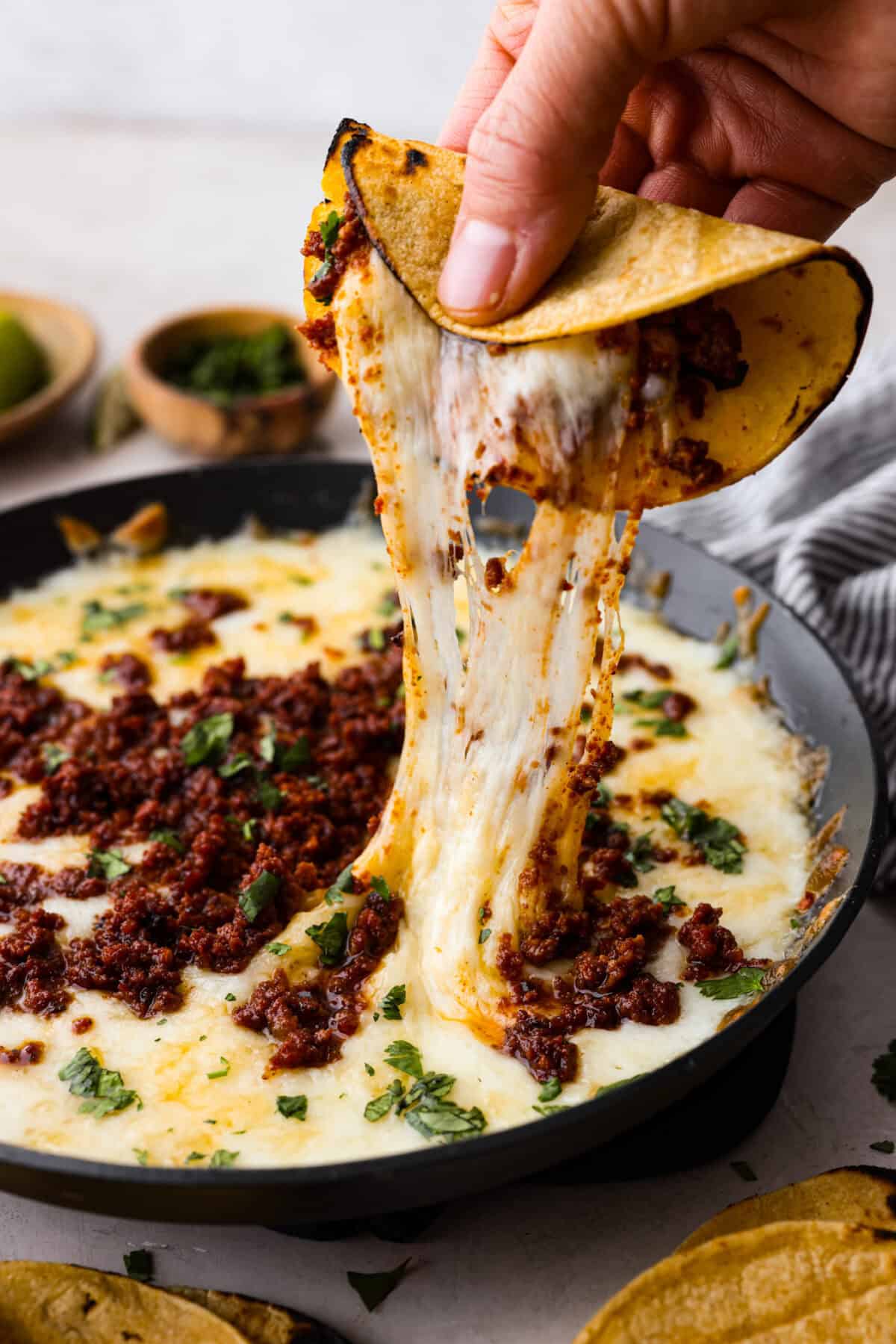Queso Fundido is a delicious cheesy appetizer with a kick from the Mexican chorizo. It's loaded with buttery, melty cheeses and covered in spicy chorizo sausage. Angle shot of stretchy queso fundido.