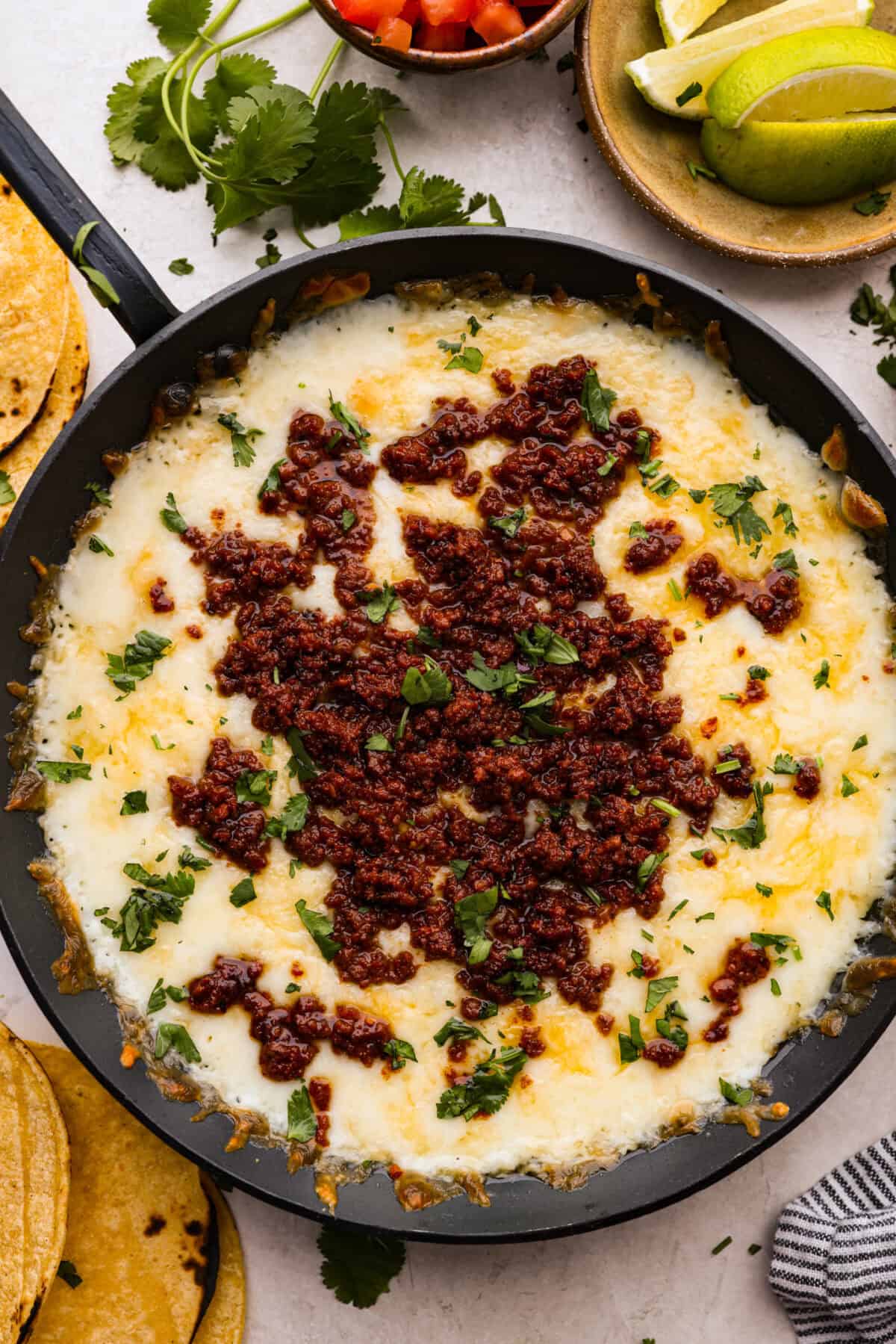 Queso Fundido is a delicious cheesy appetizer with a kick from the Mexican chorizo. It's loaded with buttery, melty cheeses and covered in spicy chorizo sausage. Overhead shot of queso fundido in a skillet.