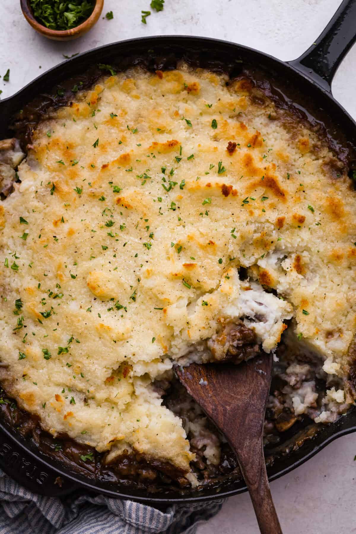 Salisbury Steak casserole is a warm and comforting savory dish. It has a thick beef gravy, tender mushrooms, and seasoned hamburger topped with rich, creamy potatoes. Overhead shot of salisbury steak casserole with a wooden serving spoon.