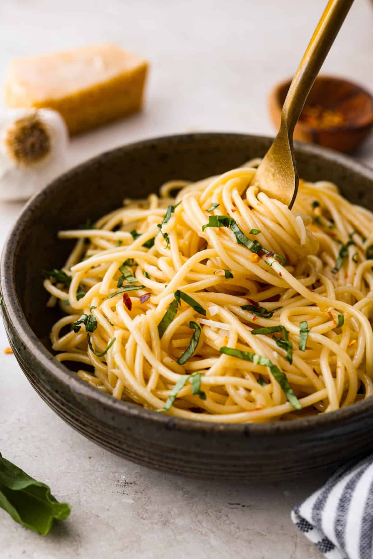 Spaghetti Aglio e Olio uses simple ingredients to create a dish bursting with flavor! With just garlic, olive oil, chili flakes, pasta, and parmesan cheese, this classic Italian recipe is a go-to for a tasty meal in less than 30 minutes. Angle shot of plated spaghetti aglio e olio with a golden fork in it.