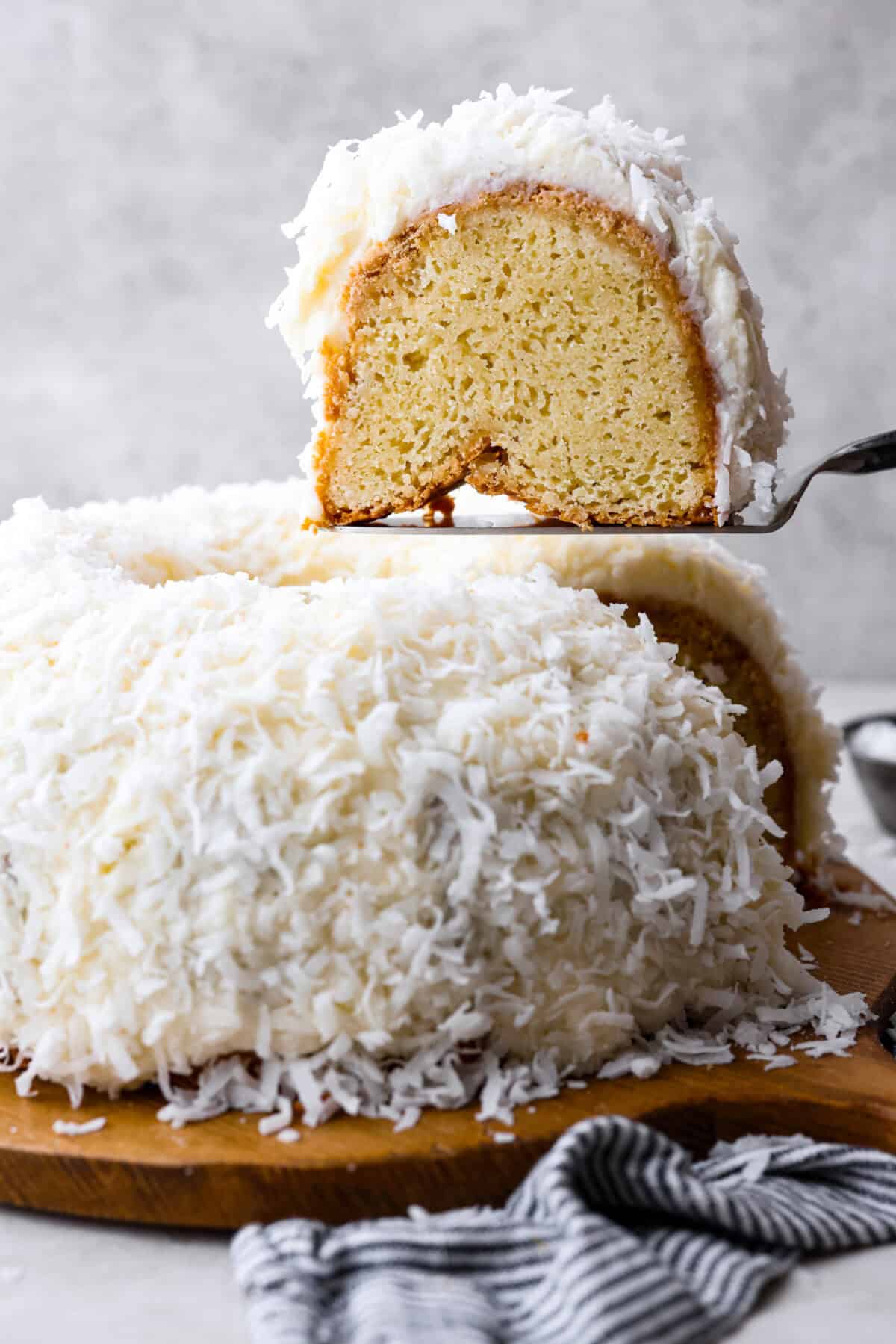 Tom Cruise coconut cake is a dense pound cake with coconut flavor and silky white chocolate throughout. The indulgent frosting is a coconut cream cheese buttercream with sweetened coconut on the outside. It's a coconut lover's dream—but a super sweet one. Side view of tom cruise coconut cake with a piece being lifted out.