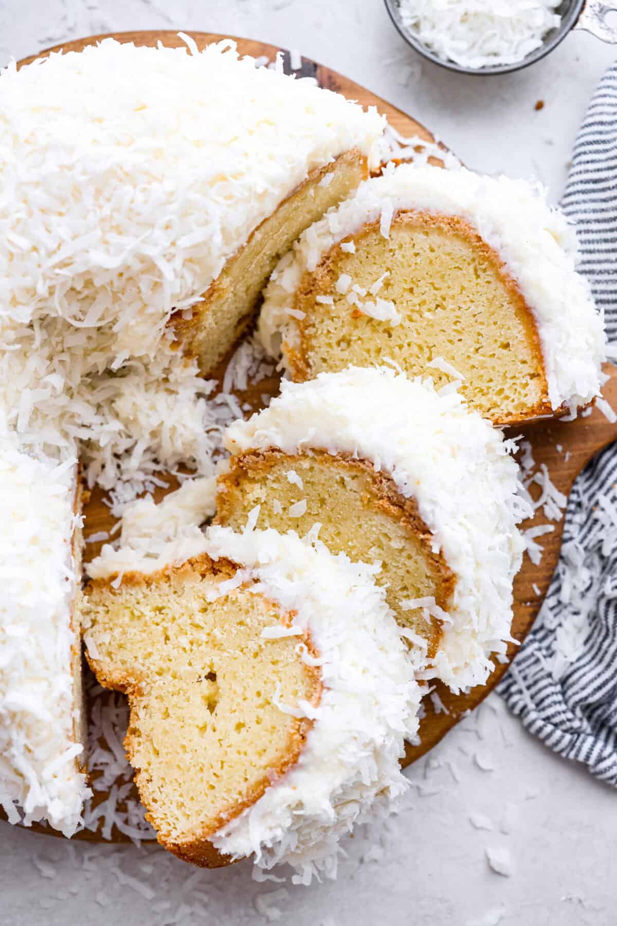 Tom Cruise coconut cake is a dense pound cake with coconut flavor and silky white chocolate throughout. The indulgent frosting is a coconut cream cheese buttercream with sweetened coconut on the outside. It's a coconut lover's dream—but a super sweet one. Overhead shot of the Tom Cruise coconut cake with a few pieces cut and turned on their side.