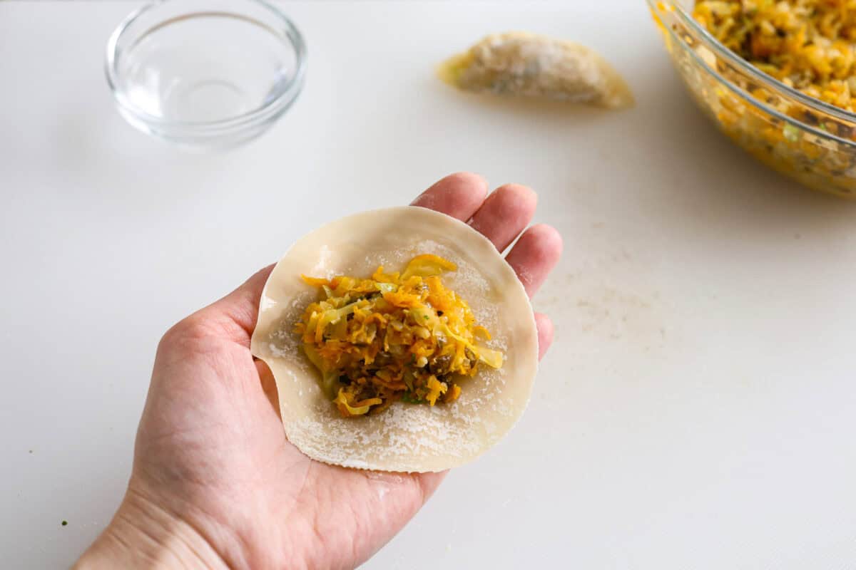 These vegetable dumplings are so full of Asian flavor, you won’t be able to stop at just one! Tender wontons are filled with an incredible veggie mixture that's infused with ginger, soy sauce, sesame oil and garlic. Like a potsticker without the meat! Angle shot of someone holding a dumpling wrapper with some of the filling in the middle.