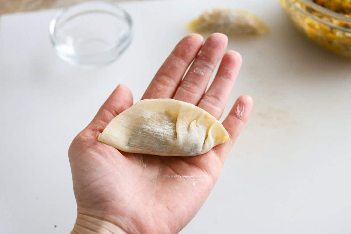 These vegetable dumplings are so full of Asian flavor, you won’t be able to stop at just one! Tender wontons are filled with an incredible veggie mixture that's infused with ginger, soy sauce, sesame oil and garlic. Like a potsticker without the meat! Overhead shot of someone holding the dumpling wrapper with filling and crimping the edges.