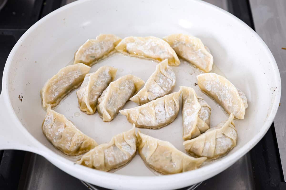 These vegetable dumplings are so full of Asian flavor, you won’t be able to stop at just one! Tender wontons are filled with an incredible veggie mixture that's infused with ginger, soy sauce, sesame oil and garlic. Like a potsticker without the meat! Angle shot of the vegetable dumplings in a skillet with hot oil.