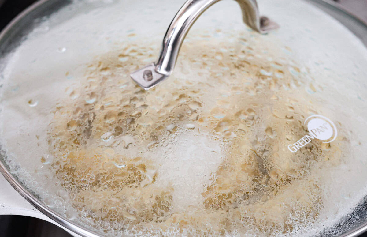 Close up shot of a lid on the skillet with the dumplings cooking inside.