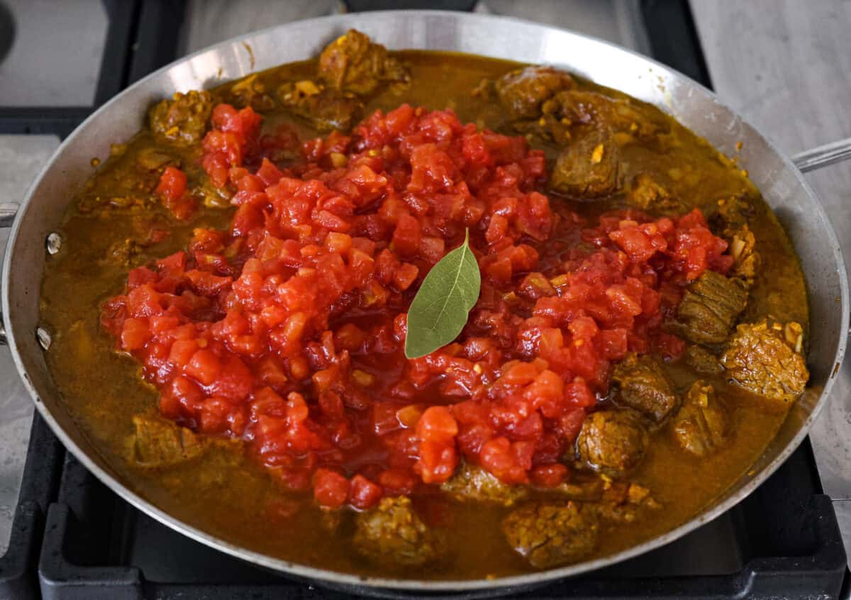 Comforting beef curry is a perfect blend of hearty and flavorful! With its mild spice level, it’s a dish that everyone can enjoy, but you can easily turn up the heat with a pinch of red pepper. Pair it with rice or naan for the ultimate cozy dinner! Angle shot of tomatoes and water added to the beef and onion mixture in the skillet.