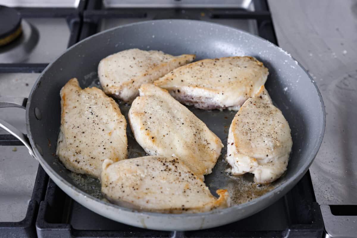 This Chicken Gloria is moist, perfectly baked chicken with a slightly seared crust. It cooks in a creamy sauce that is slightly tangy and full of flavor. It's topped with gooey cheese and makes a very satisfying meal! Angle shot of the chicken cooking in a skillet.