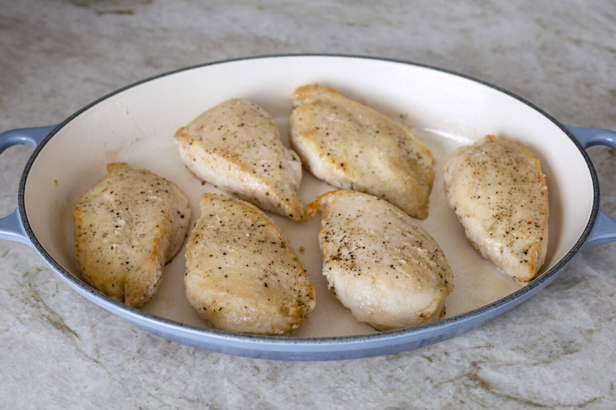 This Chicken Gloria is moist, perfectly baked chicken with a slightly seared crust. It cooks in a creamy sauce that is slightly tangy and full of flavor. It's topped with gooey cheese and makes a very satisfying meal! Angle shot browned chicken in a baking dish.