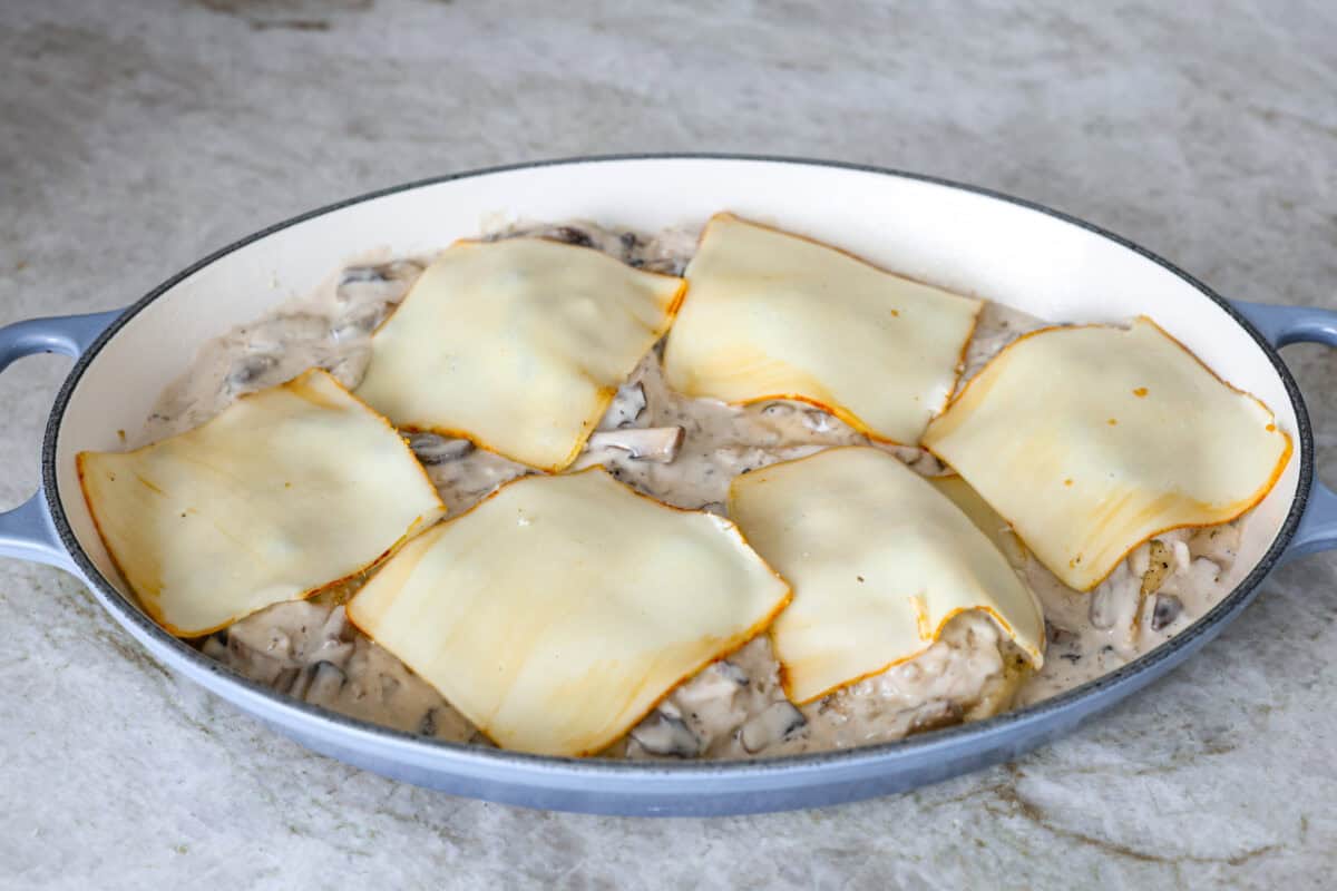 This Chicken Gloria is moist, perfectly baked chicken with a slightly seared crust. It cooks in a creamy sauce that is slightly tangy and full of flavor. It's topped with gooey cheese and makes a very satisfying meal! Angle shot of the chicken with the cream, broth and red wine vinegar in the sauce with mushrooms and broth in the baking dish covered with a slice of cheese on each chicken breast.