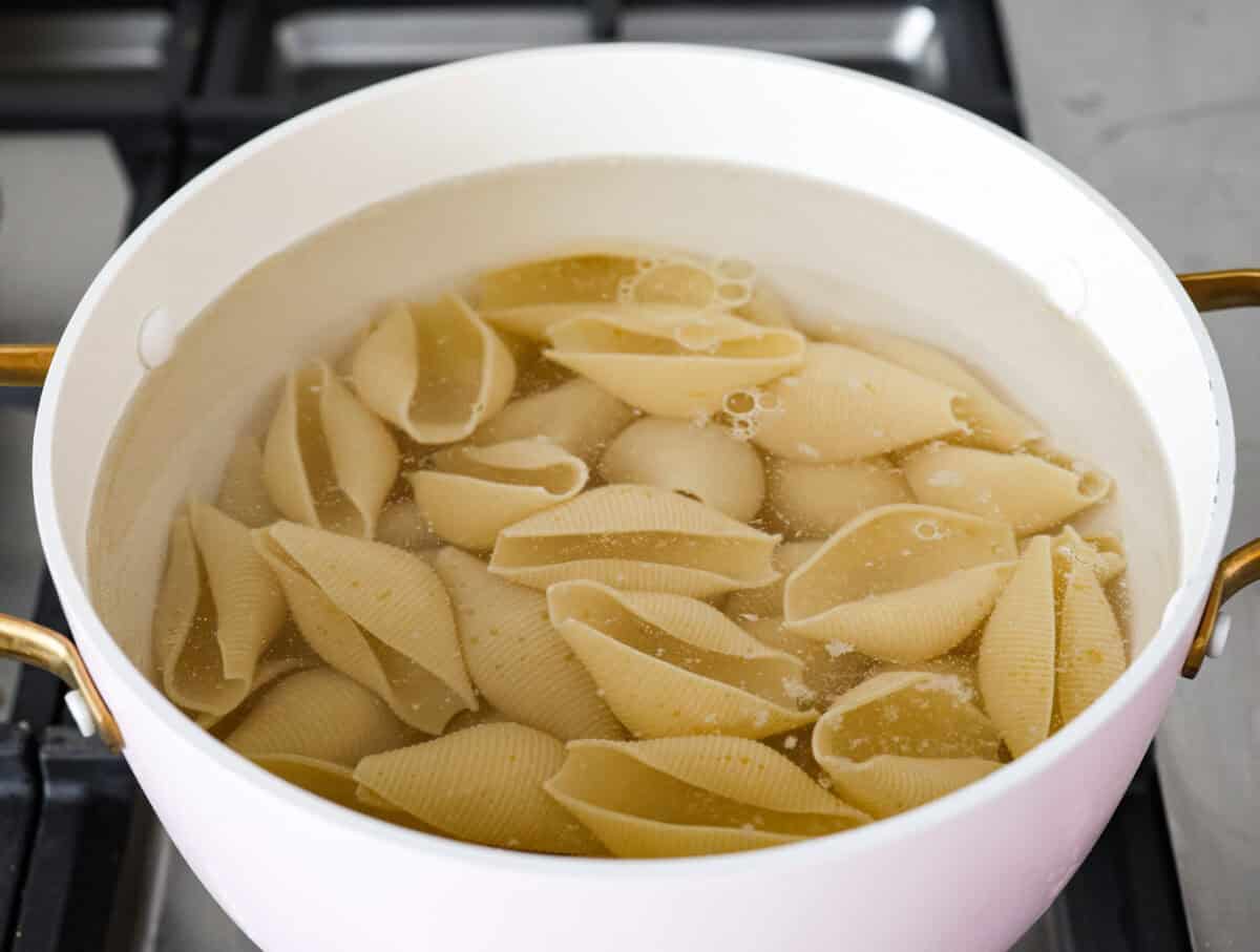 Seafood Stuffed Shells is a comforting meal that's sure to impress! Jumbo pasta shells are generously filled with a creamy, savory seafood filling and coated in a rich Alfredo-based sauce. Finish with a crispy crumb topping for an irresistible dinner! Angle shot of large pasta shells being cooked in boiling water.