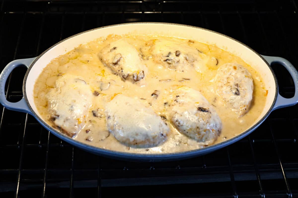 This Chicken Gloria is moist, perfectly baked chicken with a slightly seared crust. It cooks in a creamy sauce that is slightly tangy and full of flavor. It's topped with gooey cheese and makes a very satisfying meal! Angle shot of gloria chicken baking in the oven.