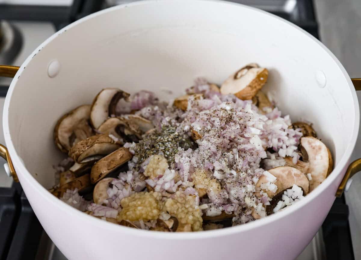 This creamy, cheesy mushroom lasagna is a delicious twist on the classic. Instead of traditional meat and red sauce, this recipe features layers of garlicky mushrooms and a rich bechamel sauce that brings incredible depth to every bite. Angle shot of mushrooms, shallots, garlic and seasonings in a pot on the stove.
