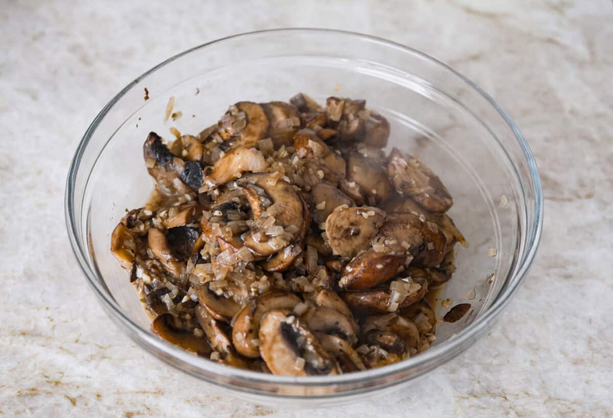 This creamy, cheesy mushroom lasagna is a delicious twist on the classic. Instead of traditional meat and red sauce, this recipe features layers of garlicky mushrooms and a rich bechamel sauce that brings incredible depth to every bite. Overhead shot of the cooked mushrooms, garlic and shallots in a bowl.