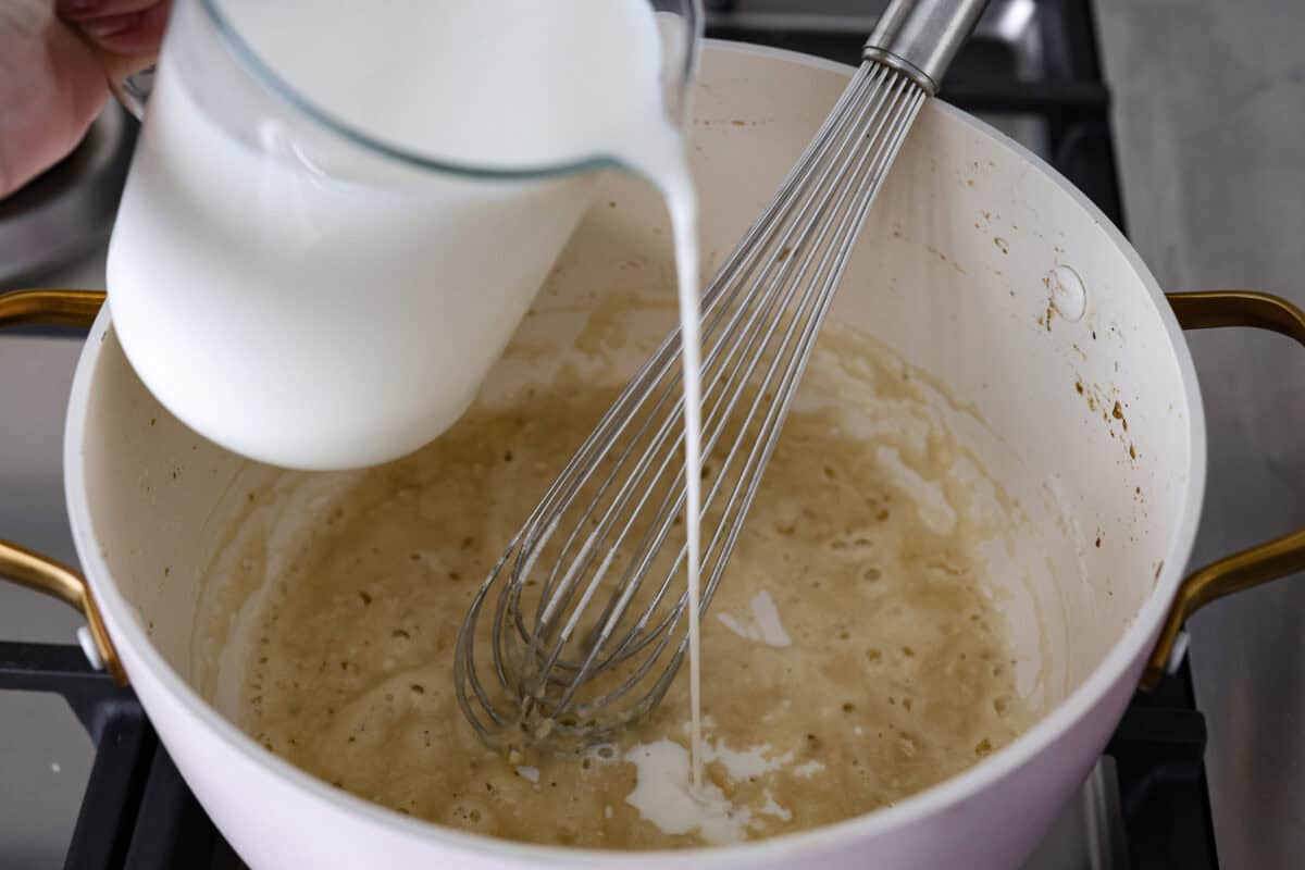 This creamy, cheesy mushroom lasagna is a delicious twist on the classic. Instead of traditional meat and red sauce, this recipe features layers of garlicky mushrooms and a rich bechamel sauce that brings incredible depth to every bite. Angle shot of someone slowly pouring milk into the roux.