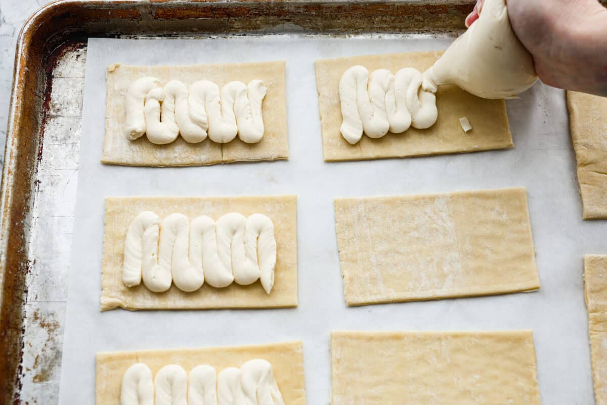 Craving the buttery goodness of a Starbucks cream cheese Danish? Now you can make it right at home! This easy copycat recipe uses flaky puff pastry and a sweet, creamy cheese filling for a treat that’s just as delicious, maybe even better! Overhead shot of someone piping the cream cheese filling onto the rectangle puff pastry.