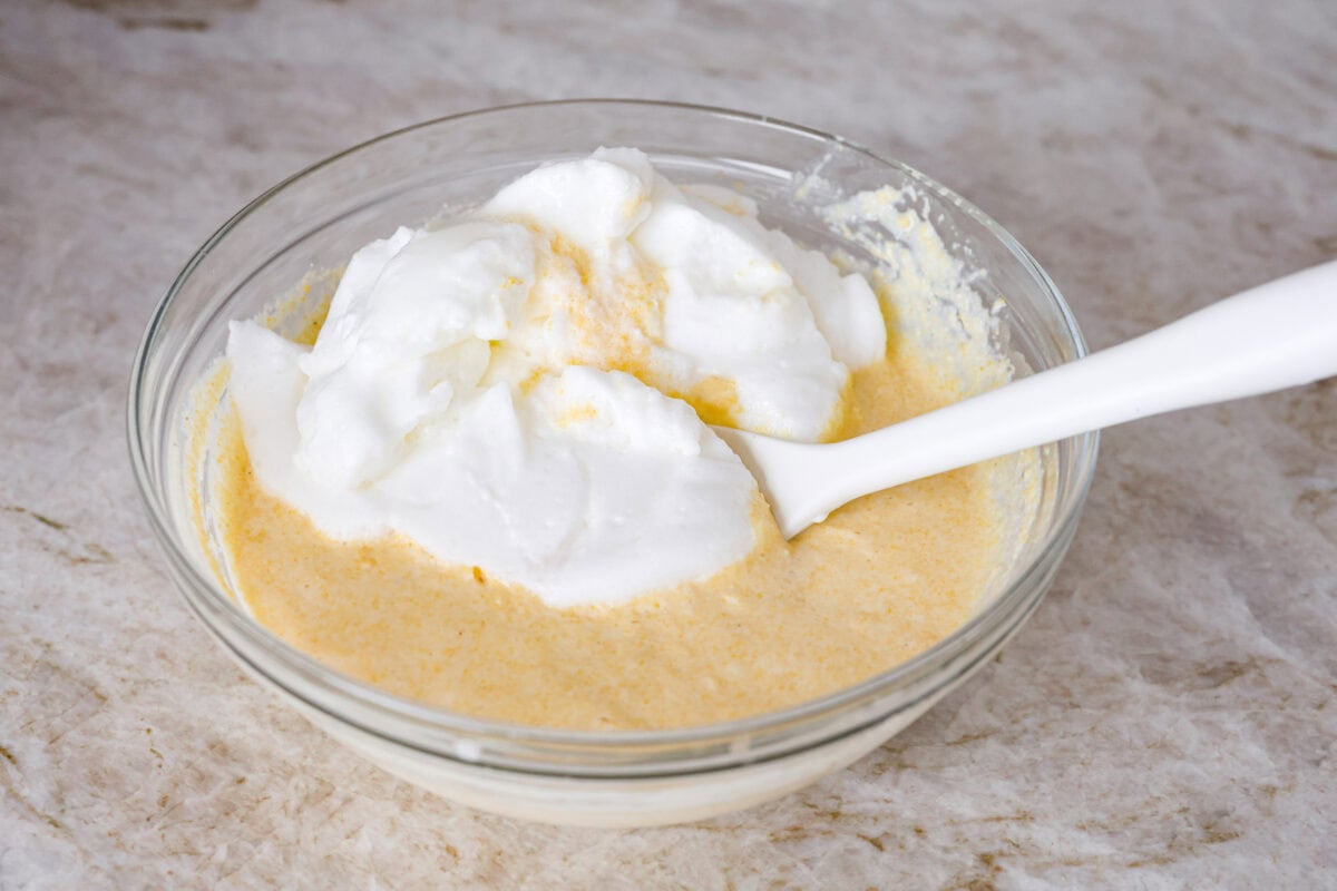 Spoon bread is a beloved classic Southern side dish. It’s similar to cornbread but is less sweet and has a softer, almost soufflé-like texture. This unique bread is best enjoyed warm with a dollop of butter, a drizzle of honey or served alongside a hearty bowl of chili. Angle shot of whipped egg whites being folded into the cornmeal mixture.