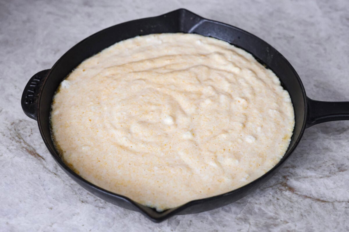Spoon bread is a beloved classic Southern side dish. It’s similar to cornbread but is less sweet and has a softer, almost soufflé-like texture. This unique bread is best enjoyed warm with a dollop of butter, a drizzle of honey or served alongside a hearty bowl of chili. Angel shot of spoon bread batter in the warmed skillet.